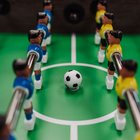 Table football game with players in blue and yellow uniforms around a black and white ball on a green field.