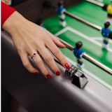 Hand with red nail polish and a ring on a foosball table